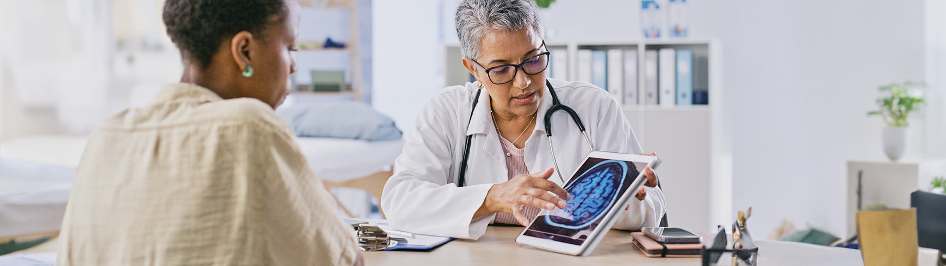 Woman and female doctor looking at image of brain scan on tablet.