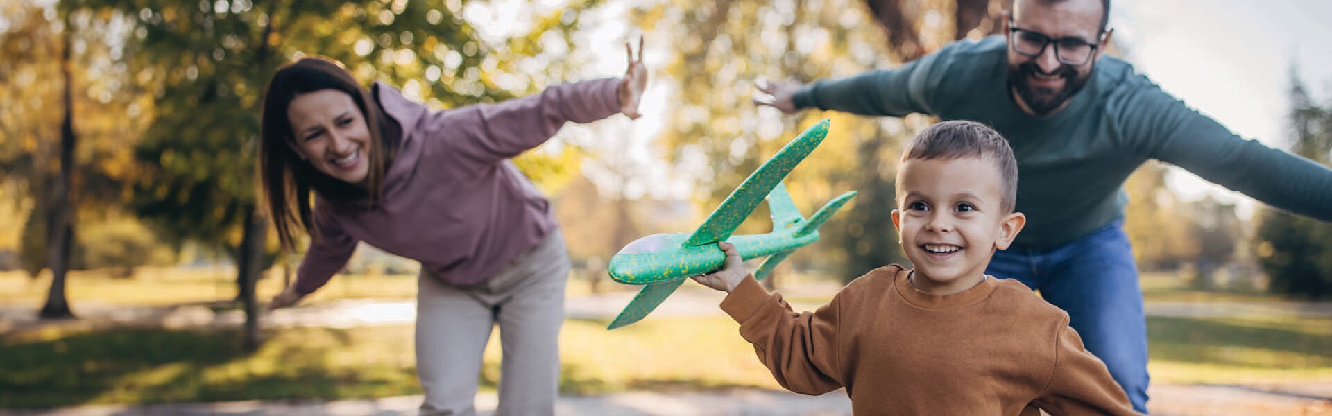 Man and woman playing outside with a young boy flying a toy airplane.