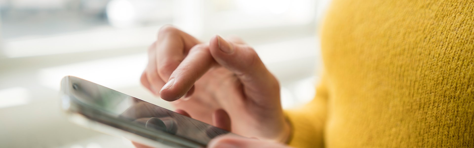 Woman in yellow sweater using cell phone.