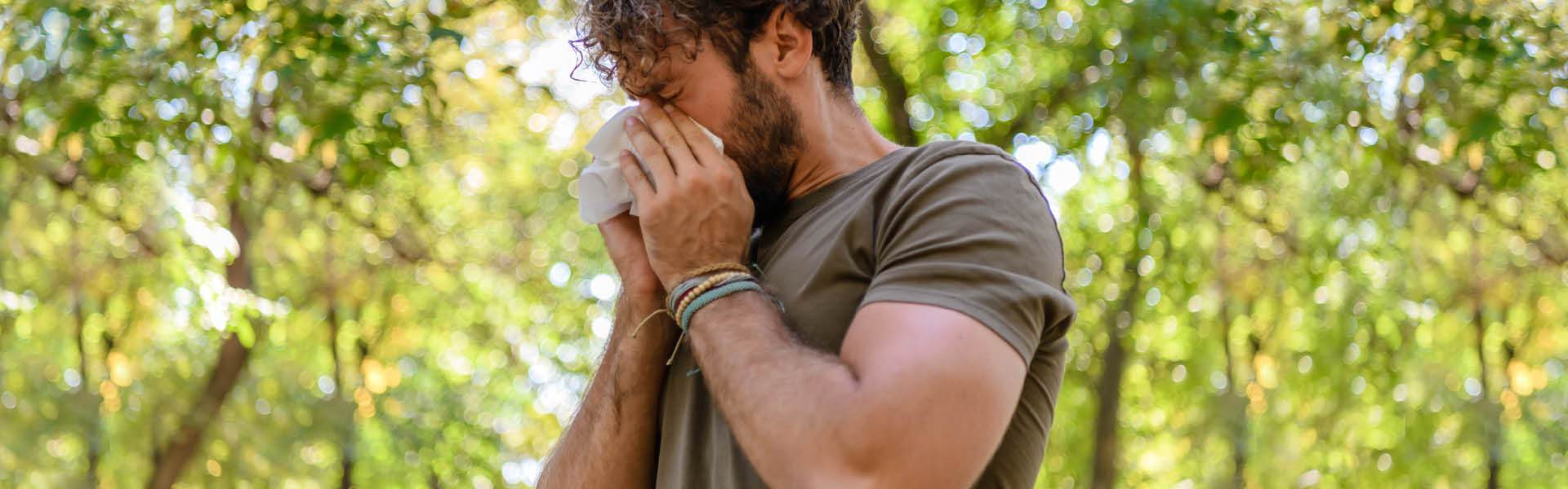 Man in a park using a tissue. 