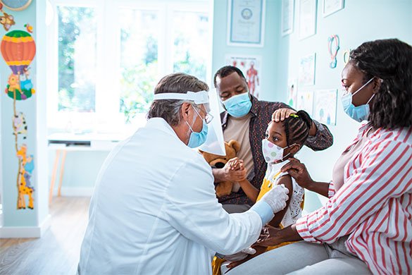 Doctor wearing mask and face shield with girl and parents wearing masks