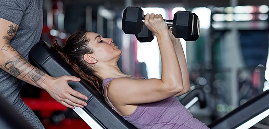 Woman in gym doing presses with hand weights.