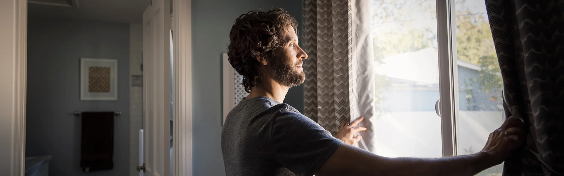 man opening window curtains to sun banner