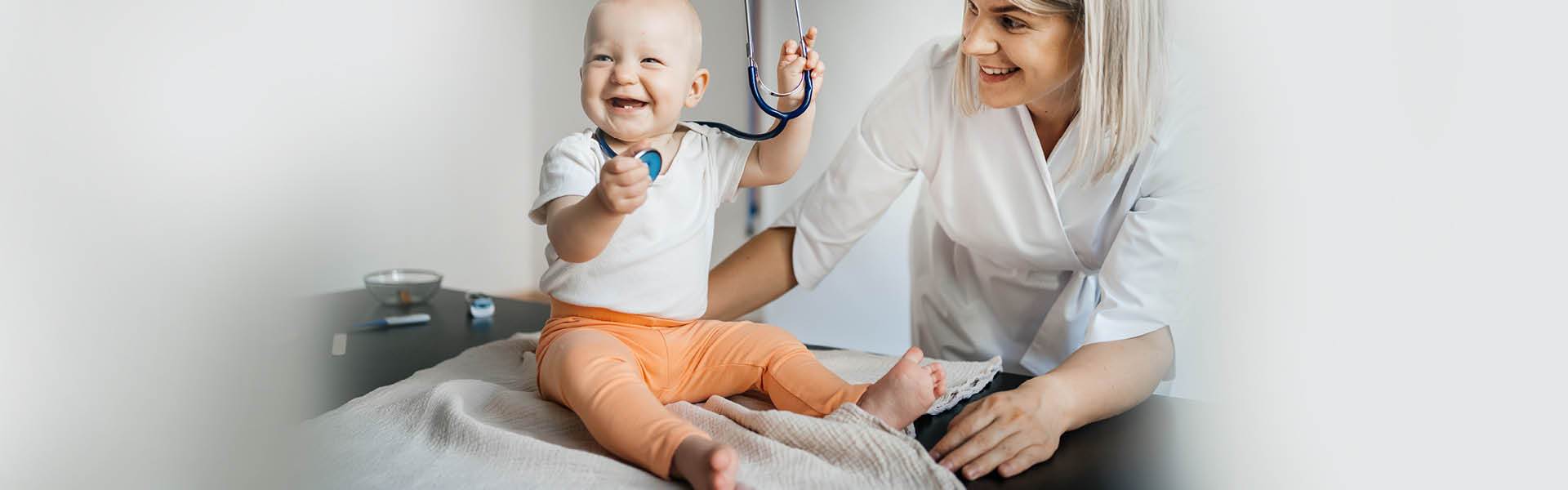 Baby on an exam table playing with a stethoscope. 