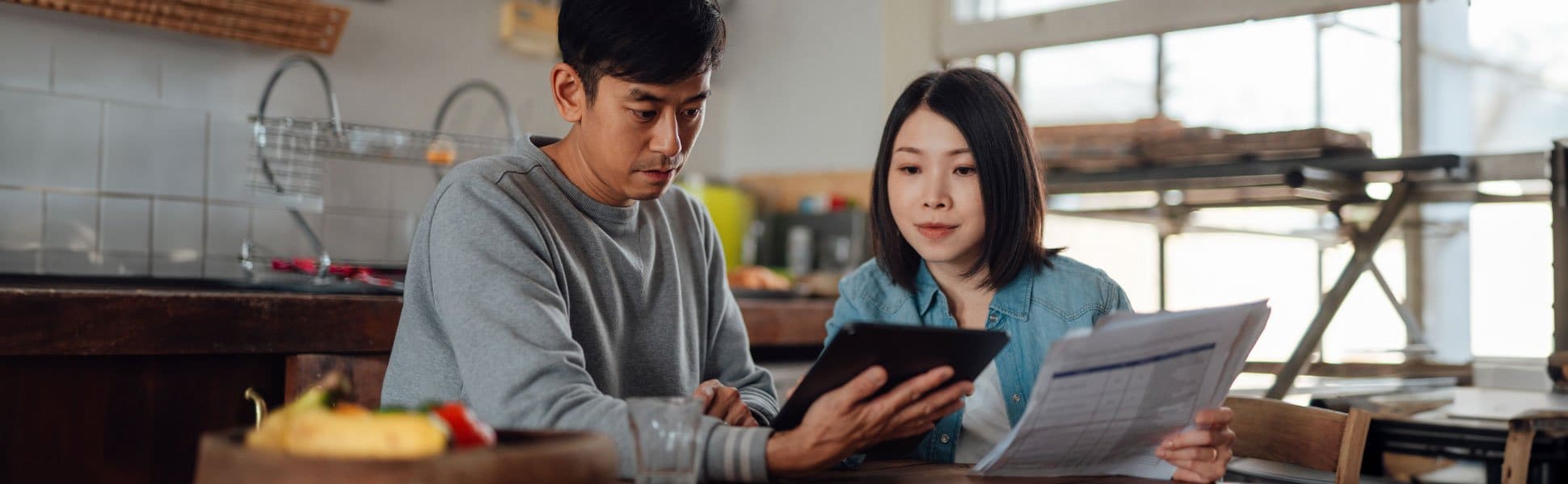 A man and woman sitting at a table looking at a tablet.