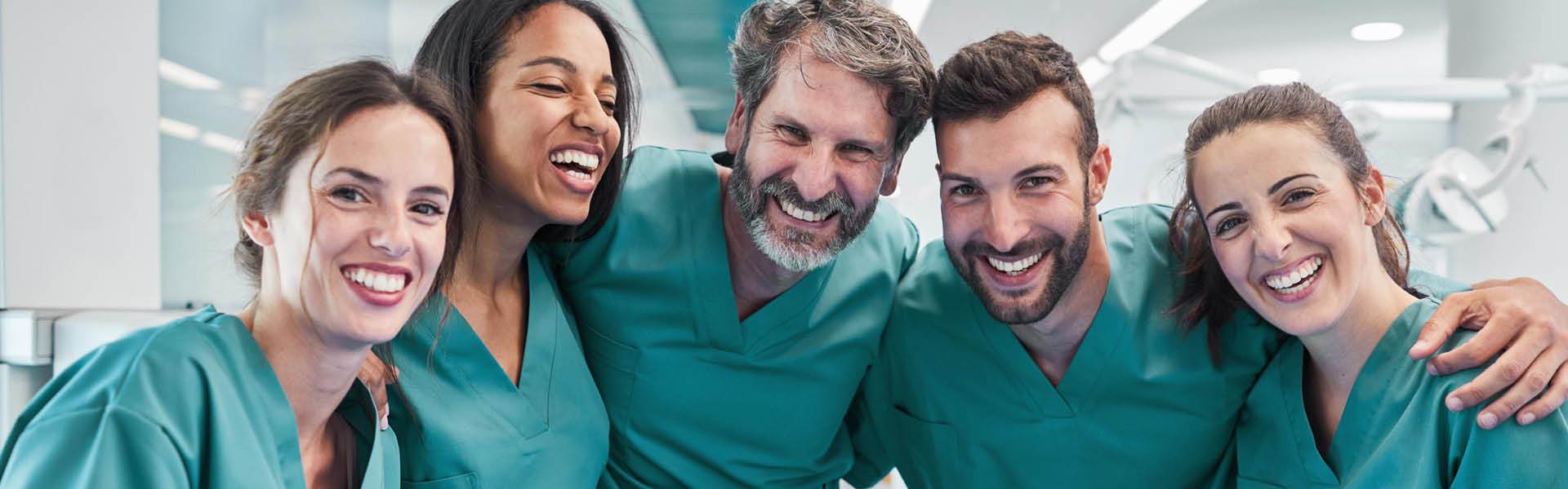 Group of smiling coworkers wearing green scrubs.